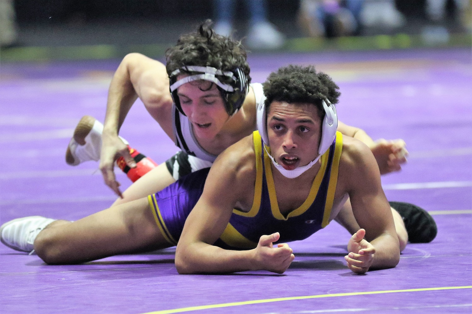 Two wrestlers in intense match on purple mat, one wearing a headgear.