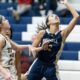 Female basketball player in blue jumps to score amid opponents.