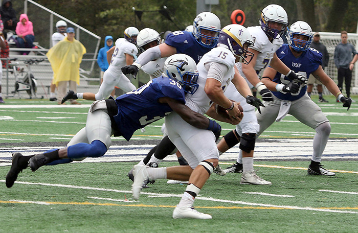 A football player in blue tackles a player in white during a game.