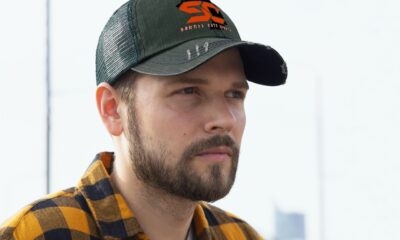 Man wearing a black cap and yellow checkered shirt looking thoughtful.