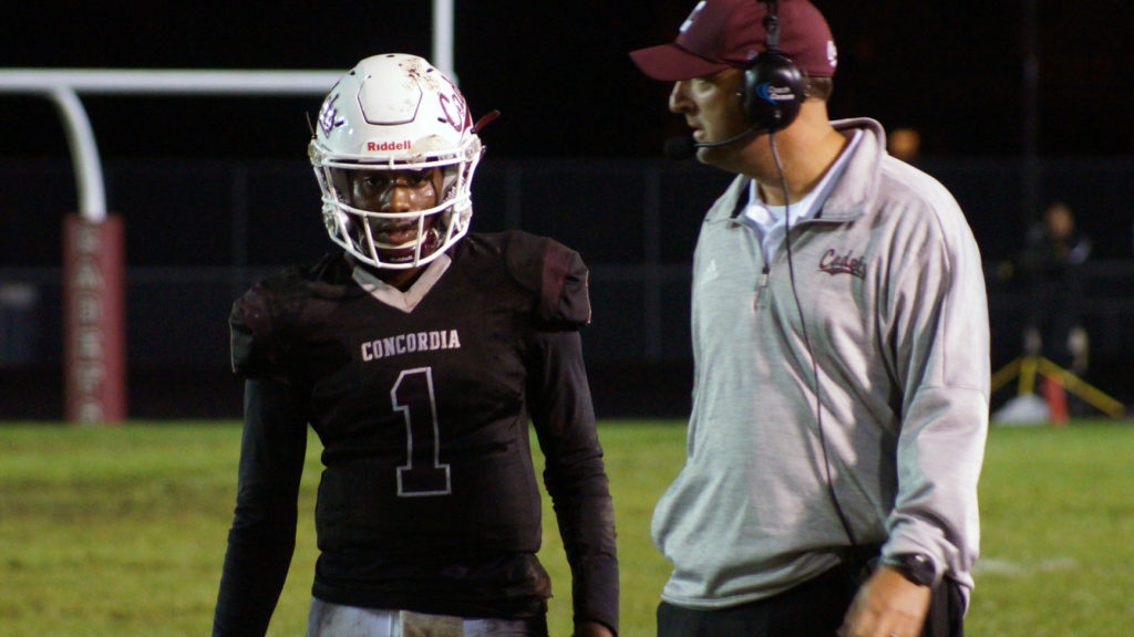 Football player wearing number 1 and coach in discussion during a night game.