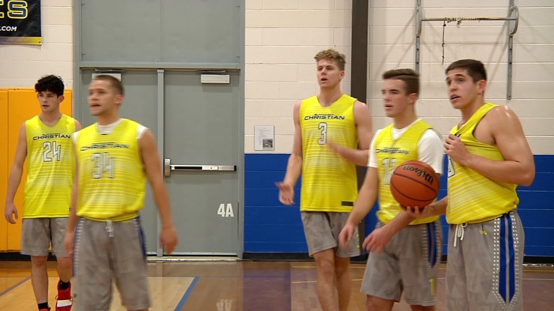 Young men playing basketball indoors in yellow jerseys.