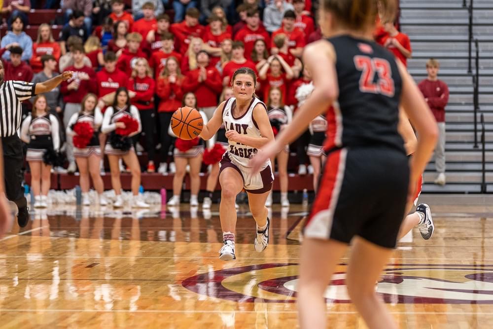 Female basketball player dribbling during a game with a crowd in the background.