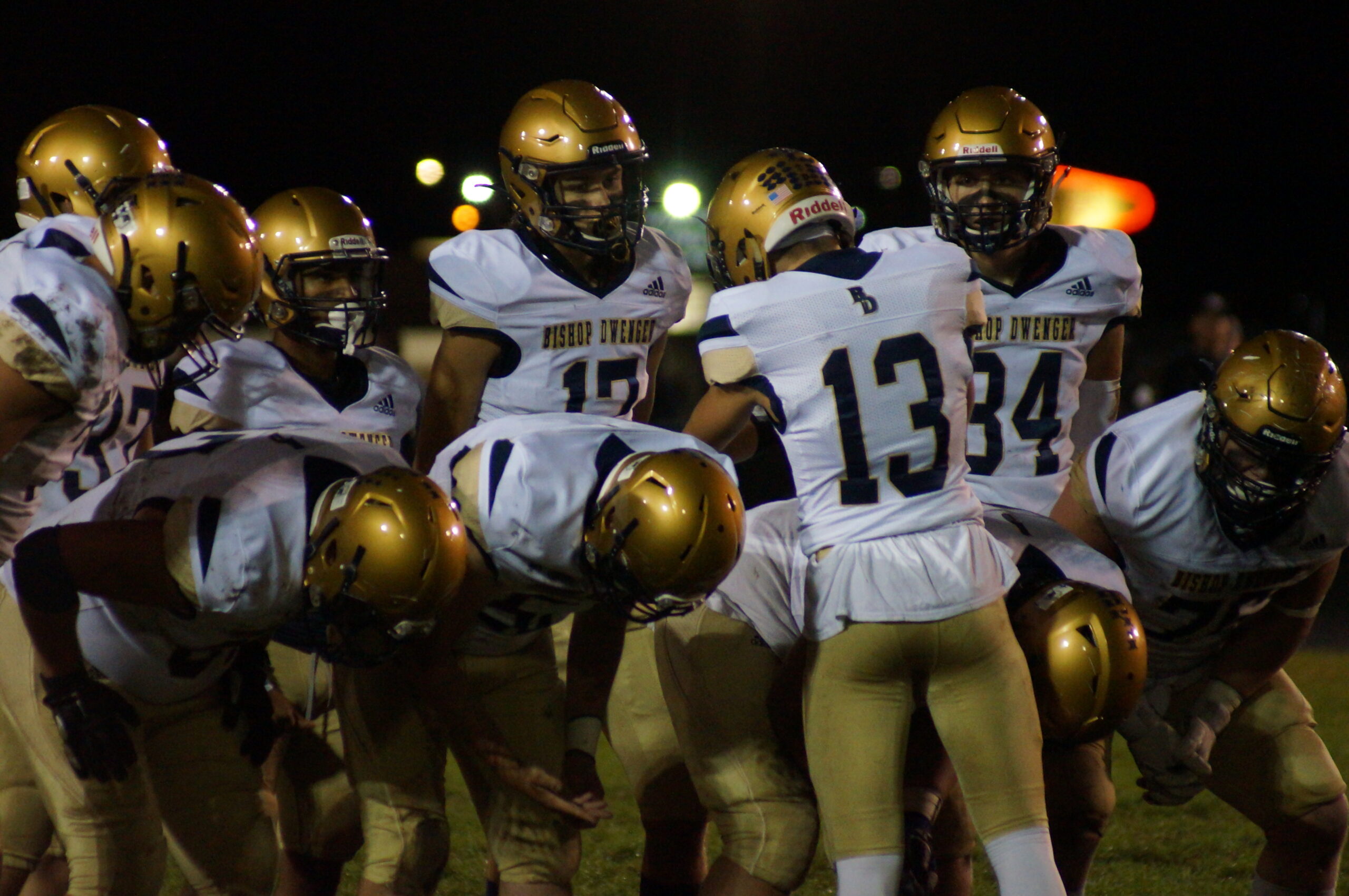 Football players in gold helmets celebrate on the field at night.