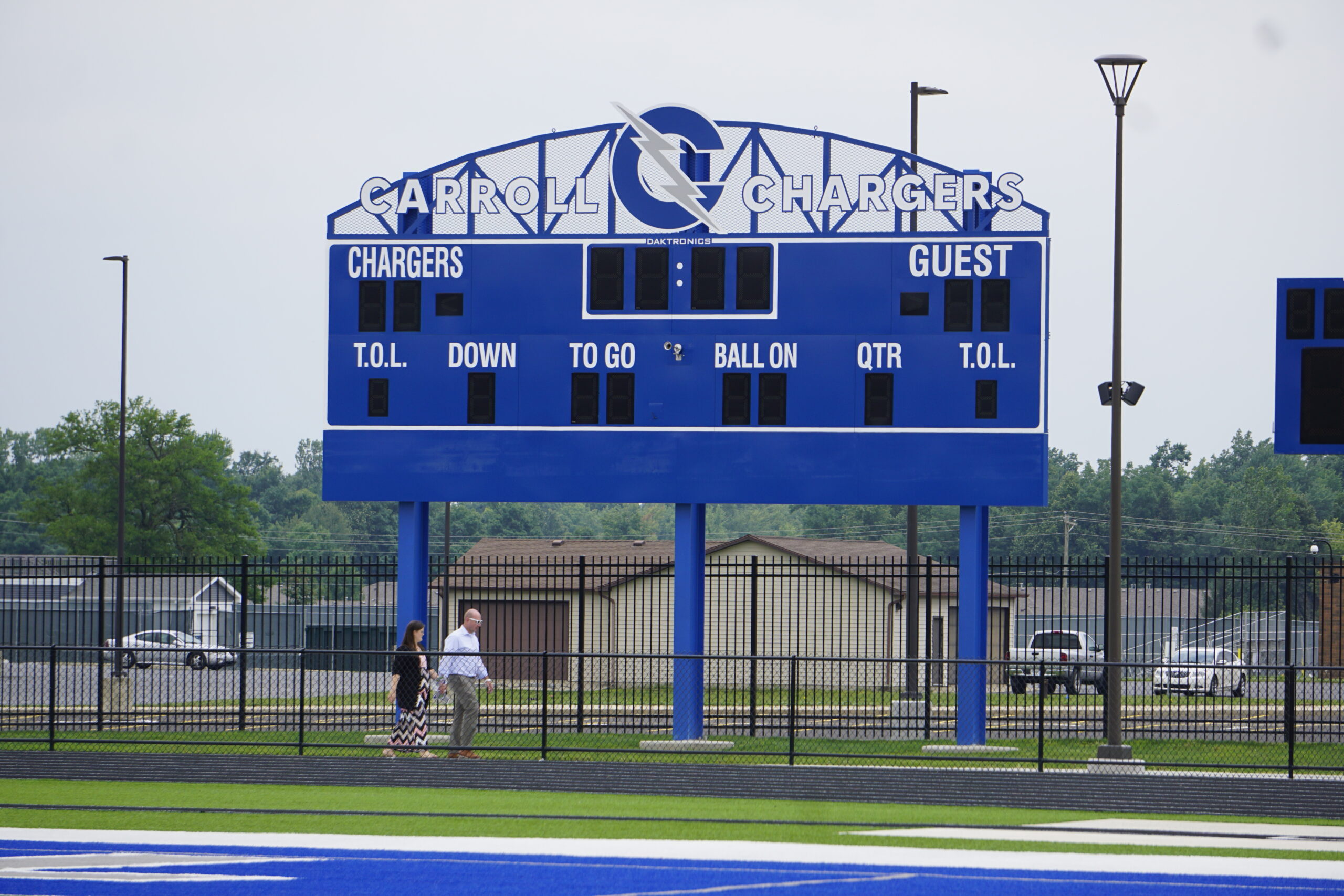 Blue football scoreboard on a field under an overcast sky.