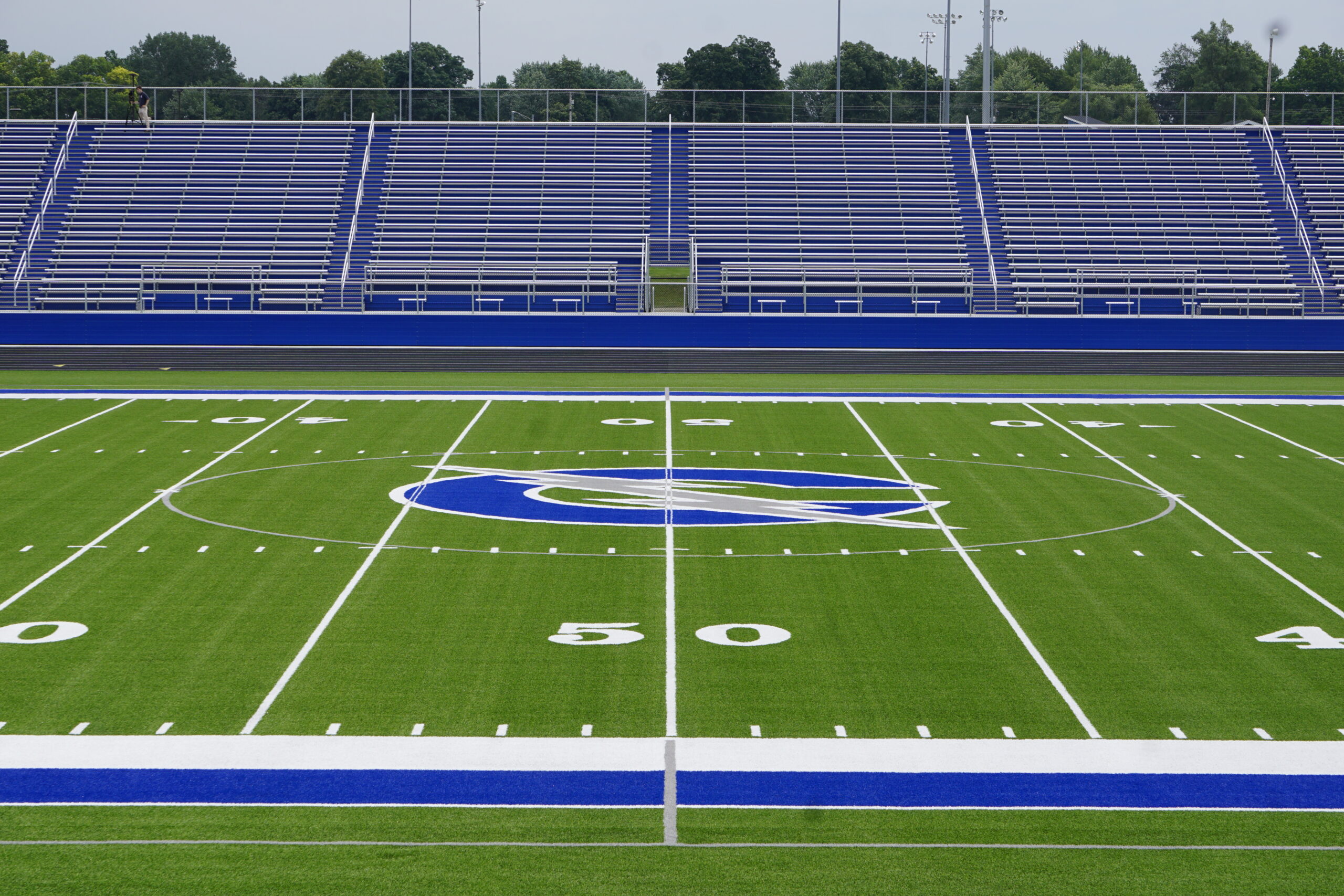 Empty football field with blue bleachers and a large team logo at midfield.