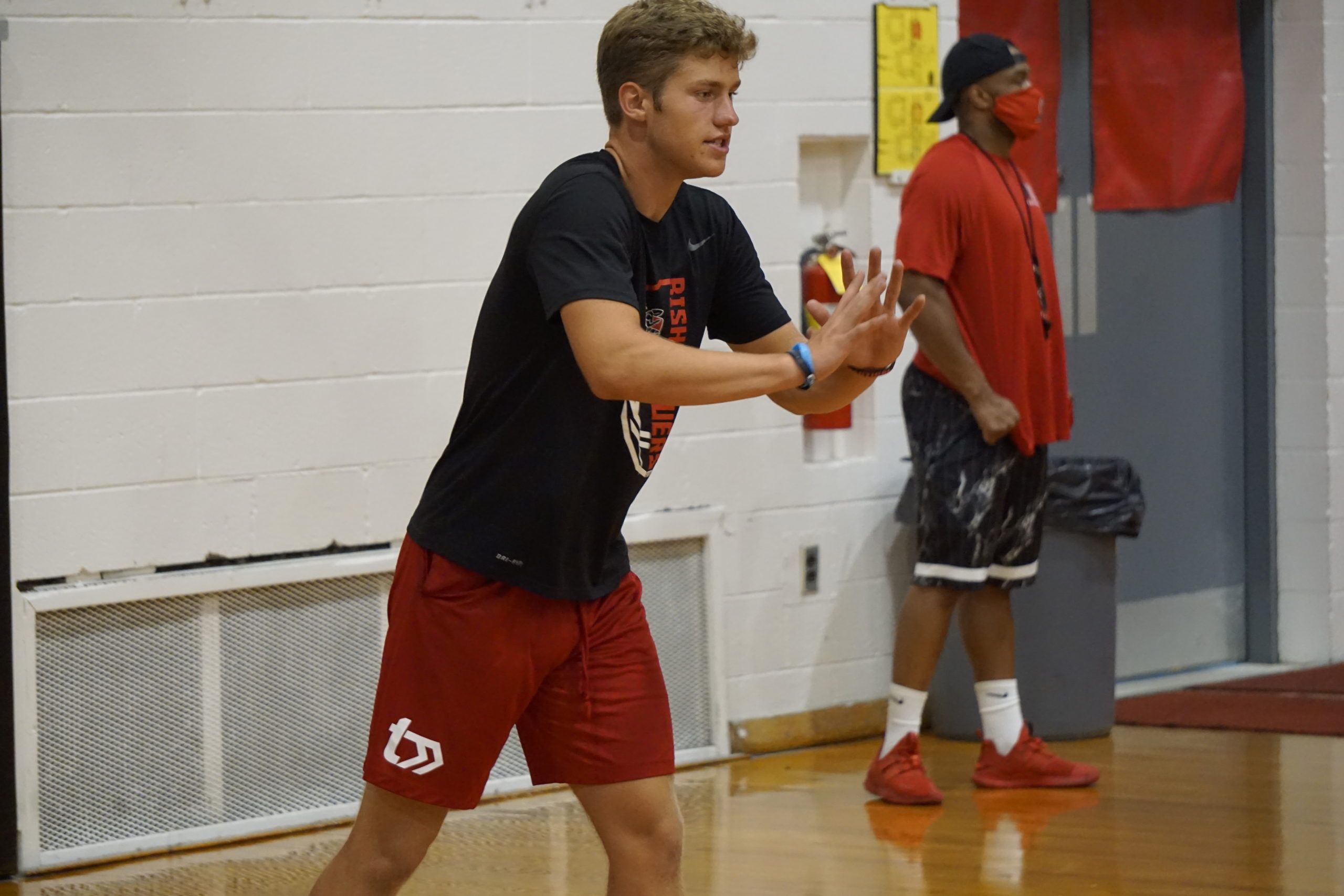 Young man in red shorts practicing basketball dribbling indoors.