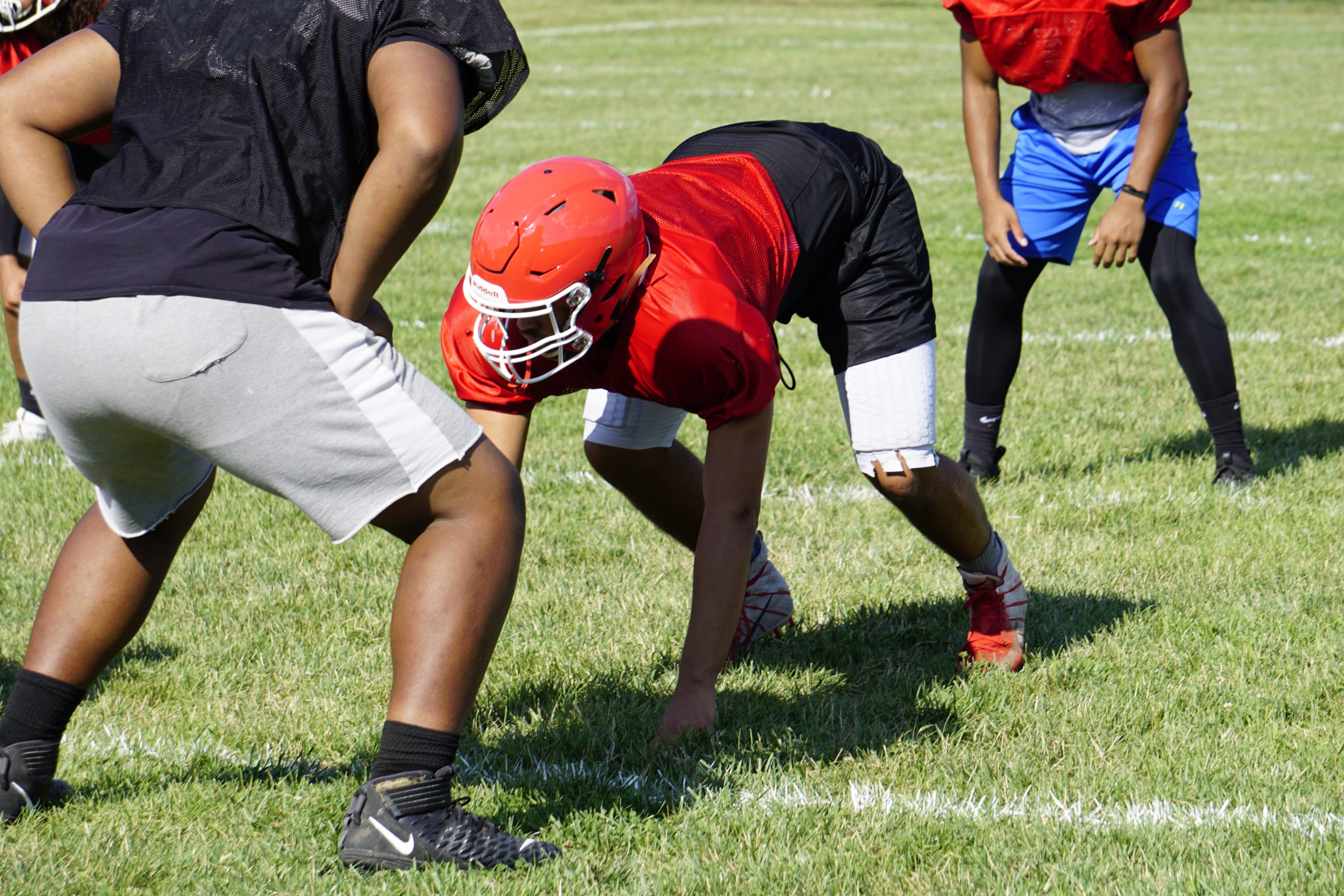 Young football player in red helmet preparing to snap the ball on a grassy field.