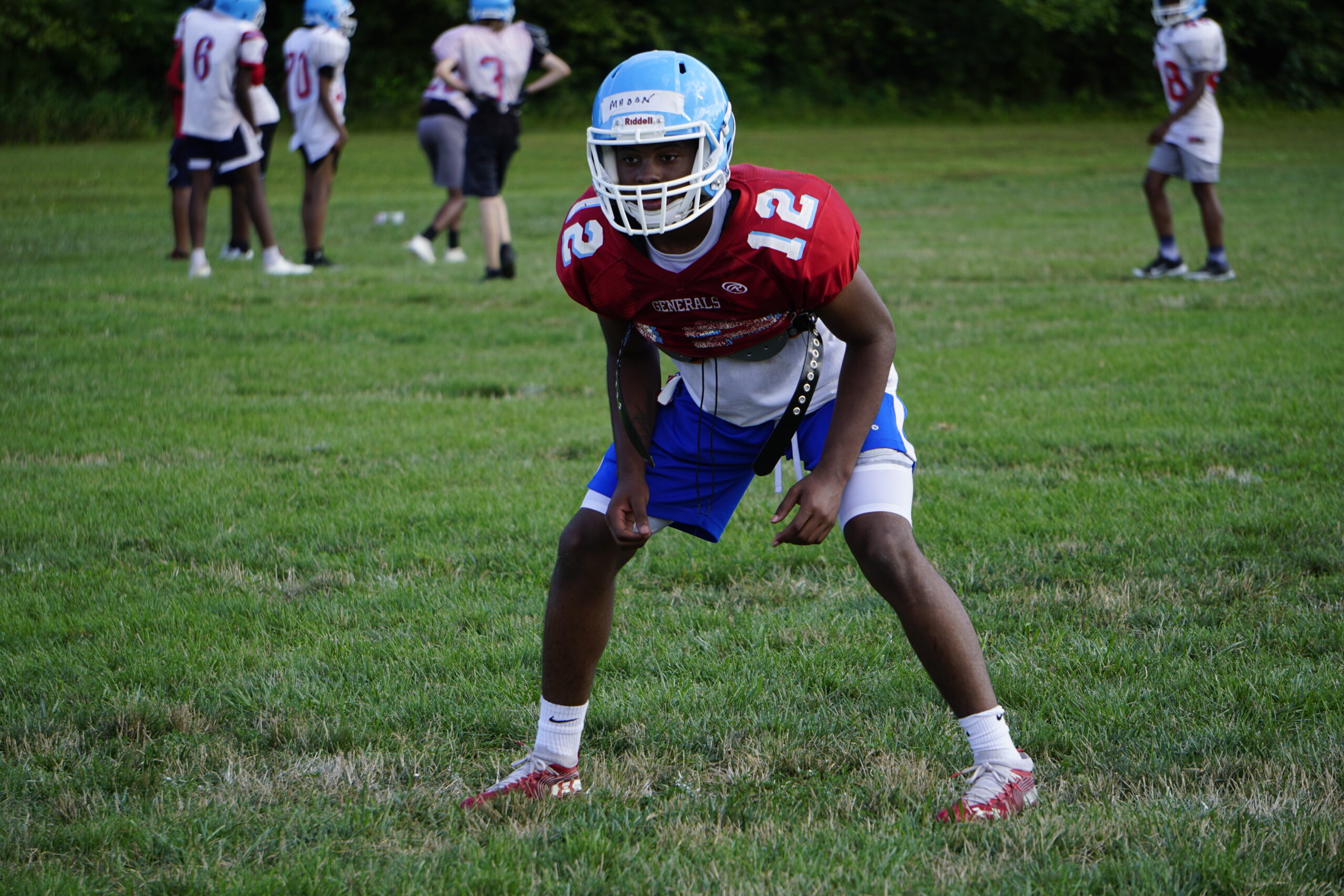 Football player in red jersey and blue shorts ready on the field.