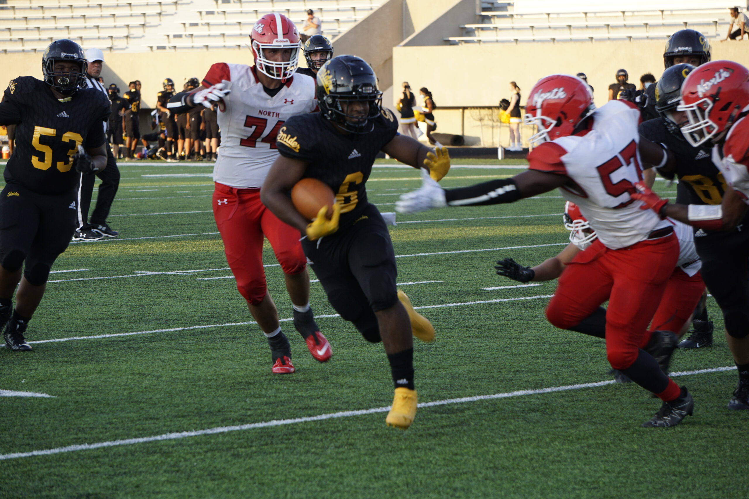 Football player in black evades defenders on the field.