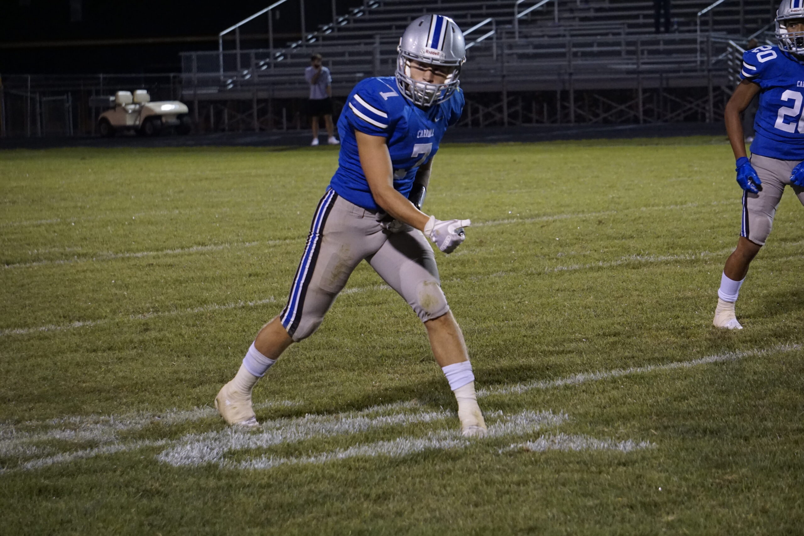 Football player in blue jersey walking on the field at night.
