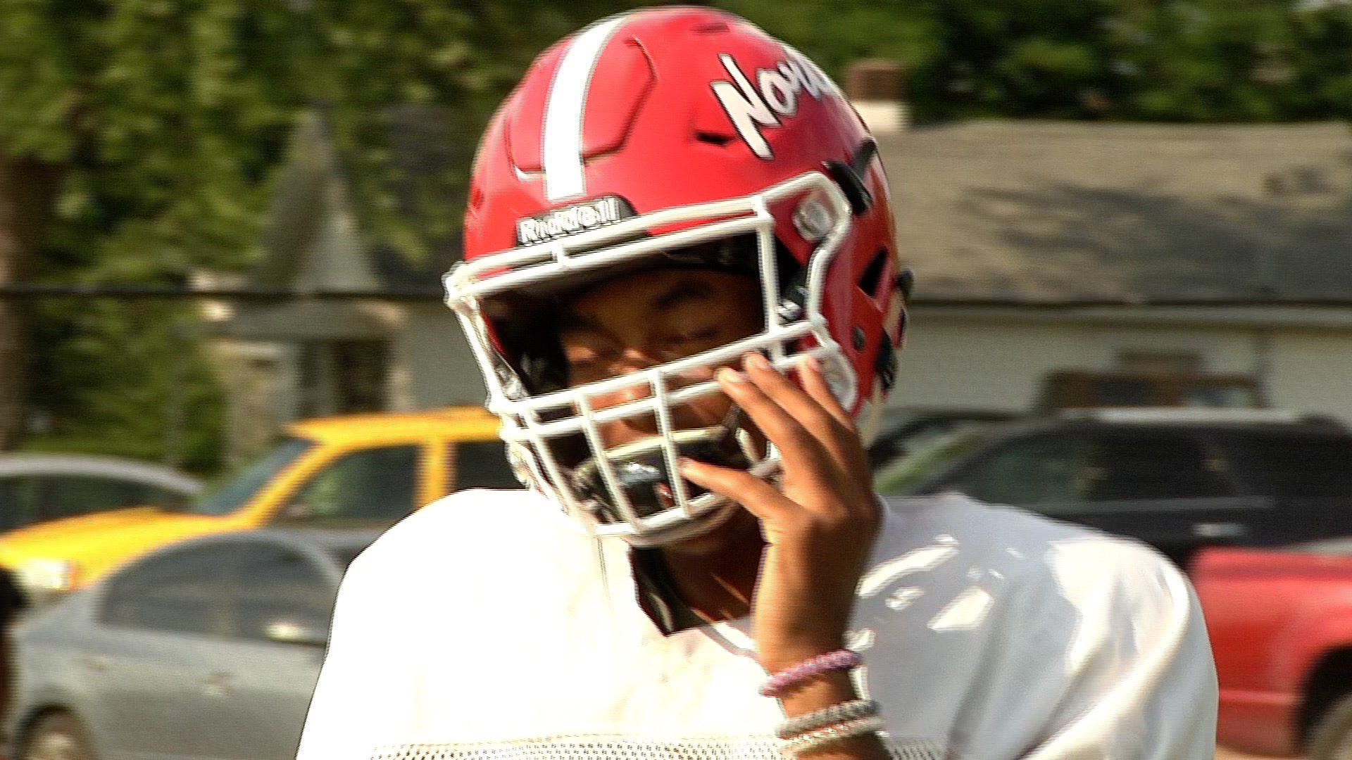 Football player in a red helmet adjusting his faceguard.