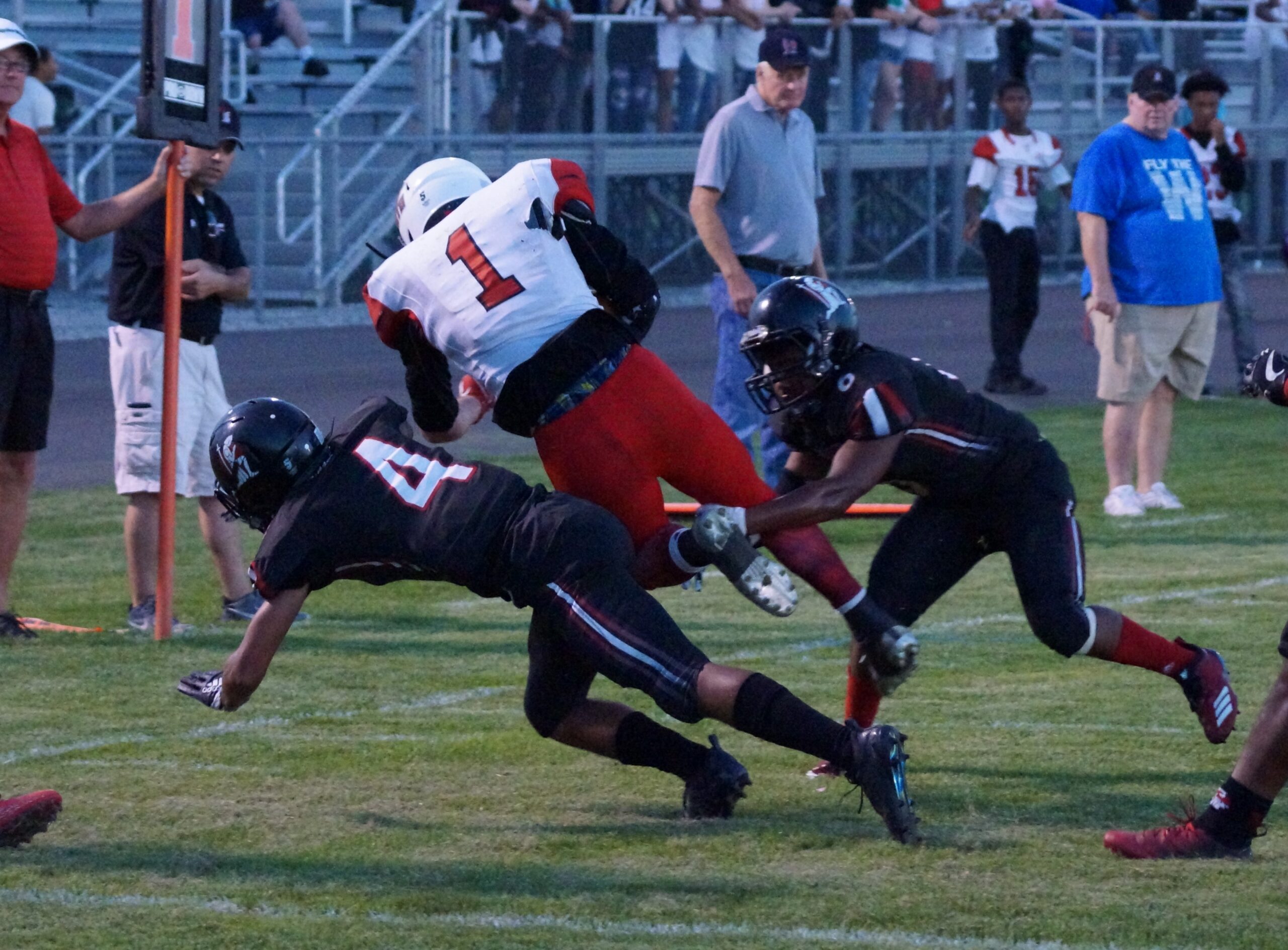 Football player in red tackled by two opponents in black uniforms.