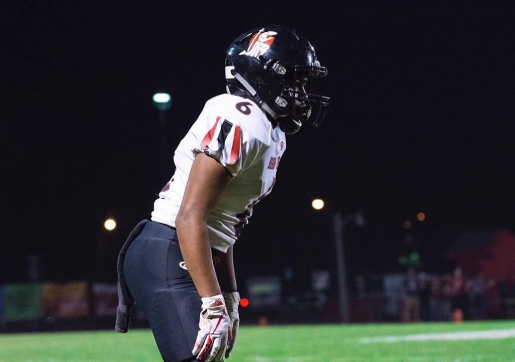 High school football player in action at night under stadium lights.