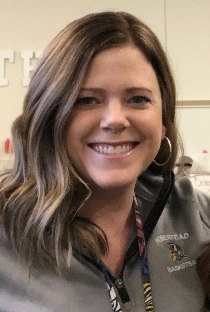Smiling woman with wavy hair and a badge, indoors.