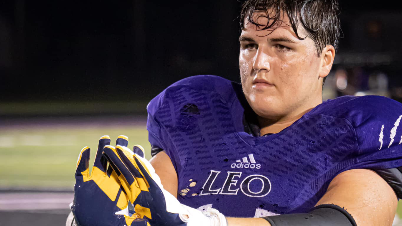 Close-up of a focused football player in purple Leo uniform and gloves.