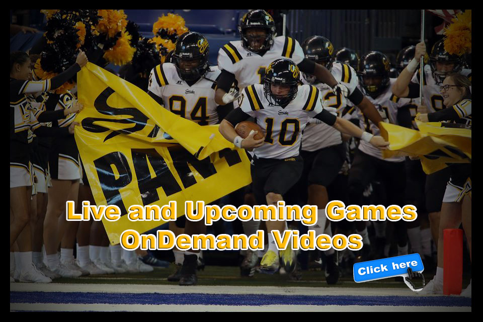 Football players running onto the field behind a yellow banner.