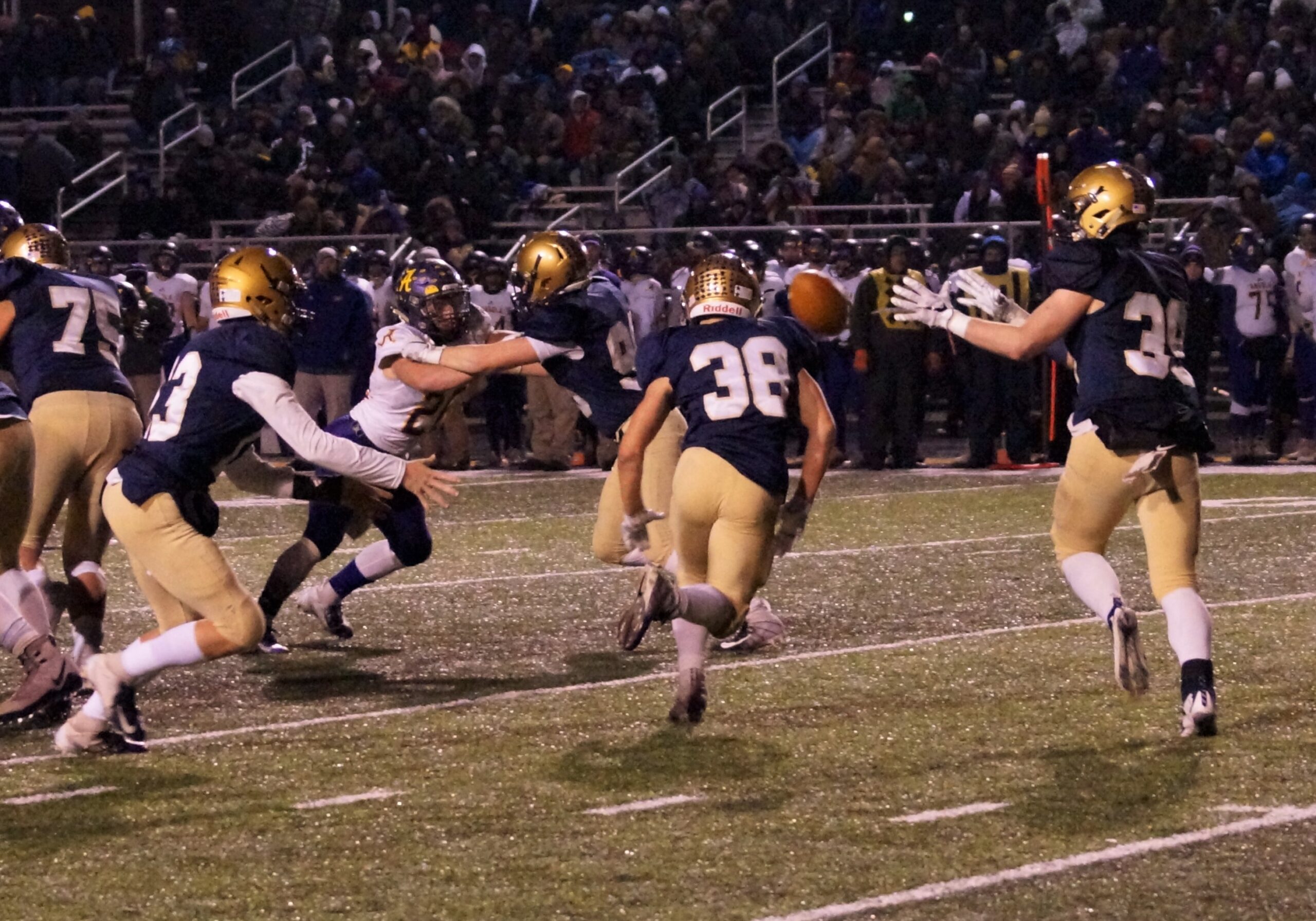 High school football players in action during a night game under stadium lights.