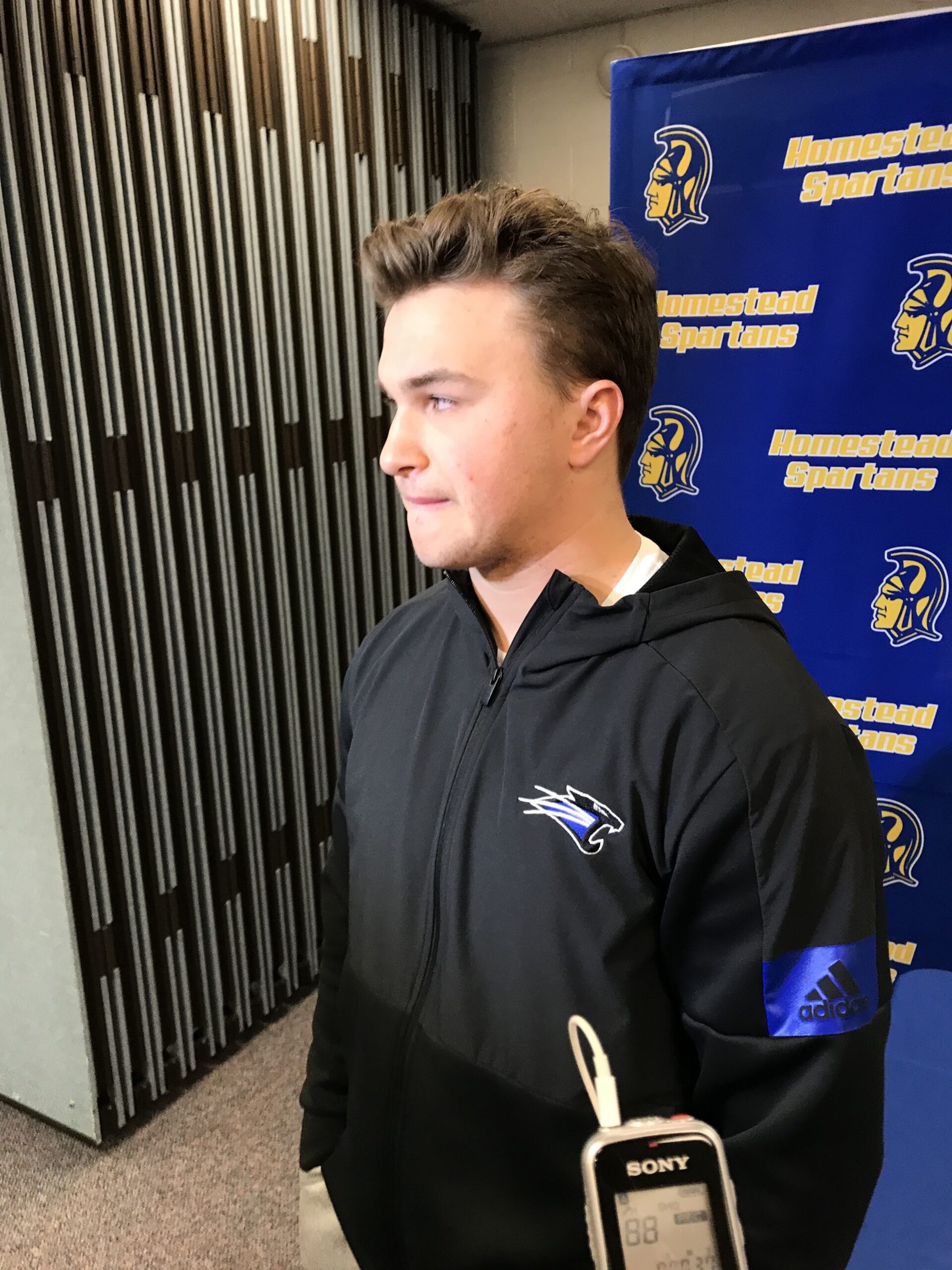 Young man in a black hoodie standing near a metal gate.