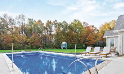 A serene backyard with a blue swimming pool surrounded by lounge chairs and autumn trees.
